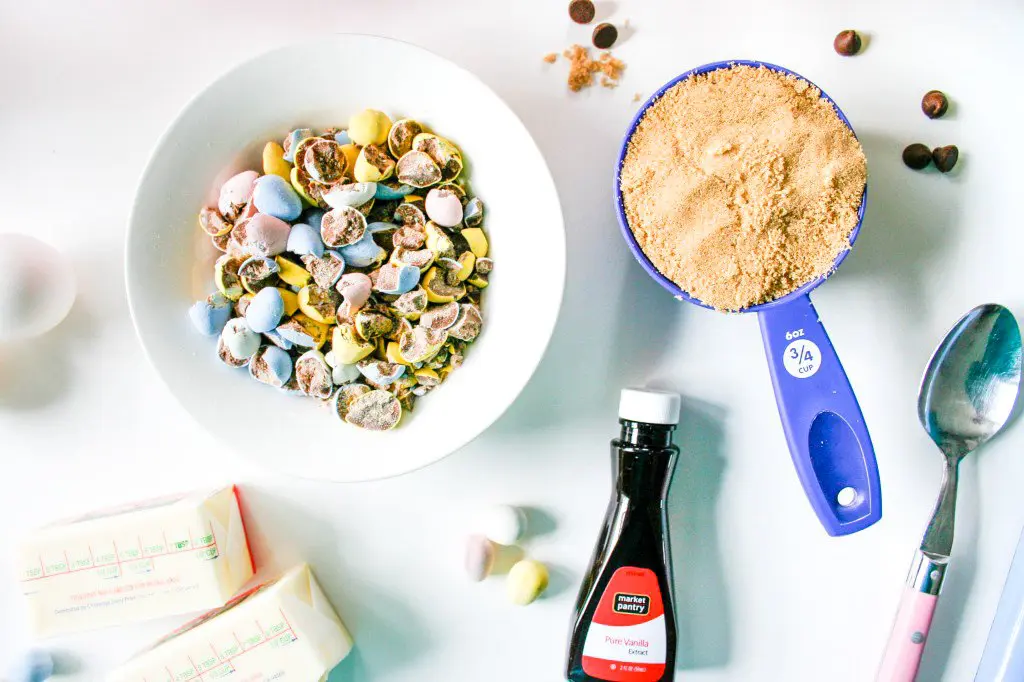 Crushed Cadbury Mini Eggs in a bowl, measuring cup of brown sugar, and container of vanilla extract