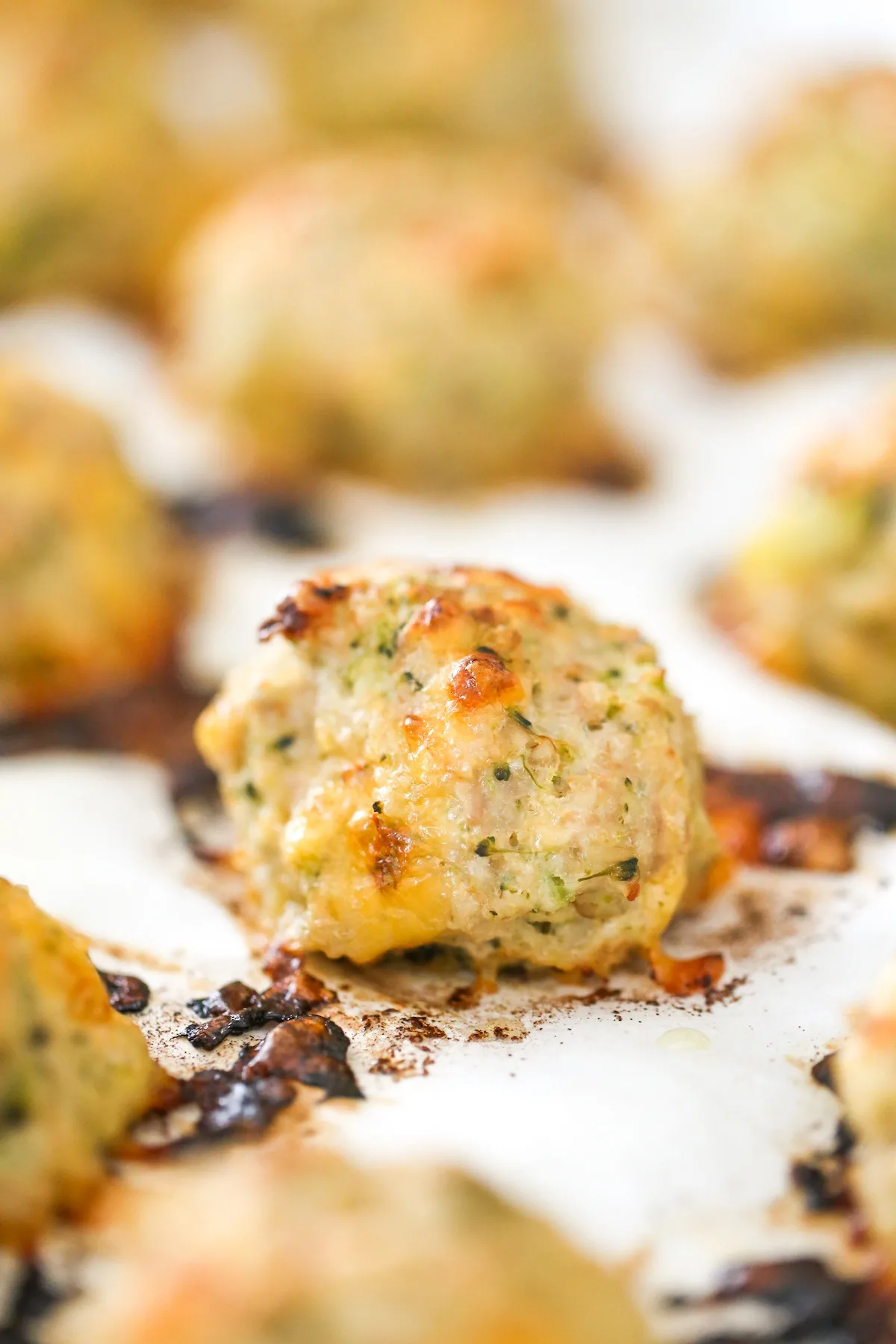 Close up of baked turkey meatballs with broccoli and cheddar cheese on a baking sheet