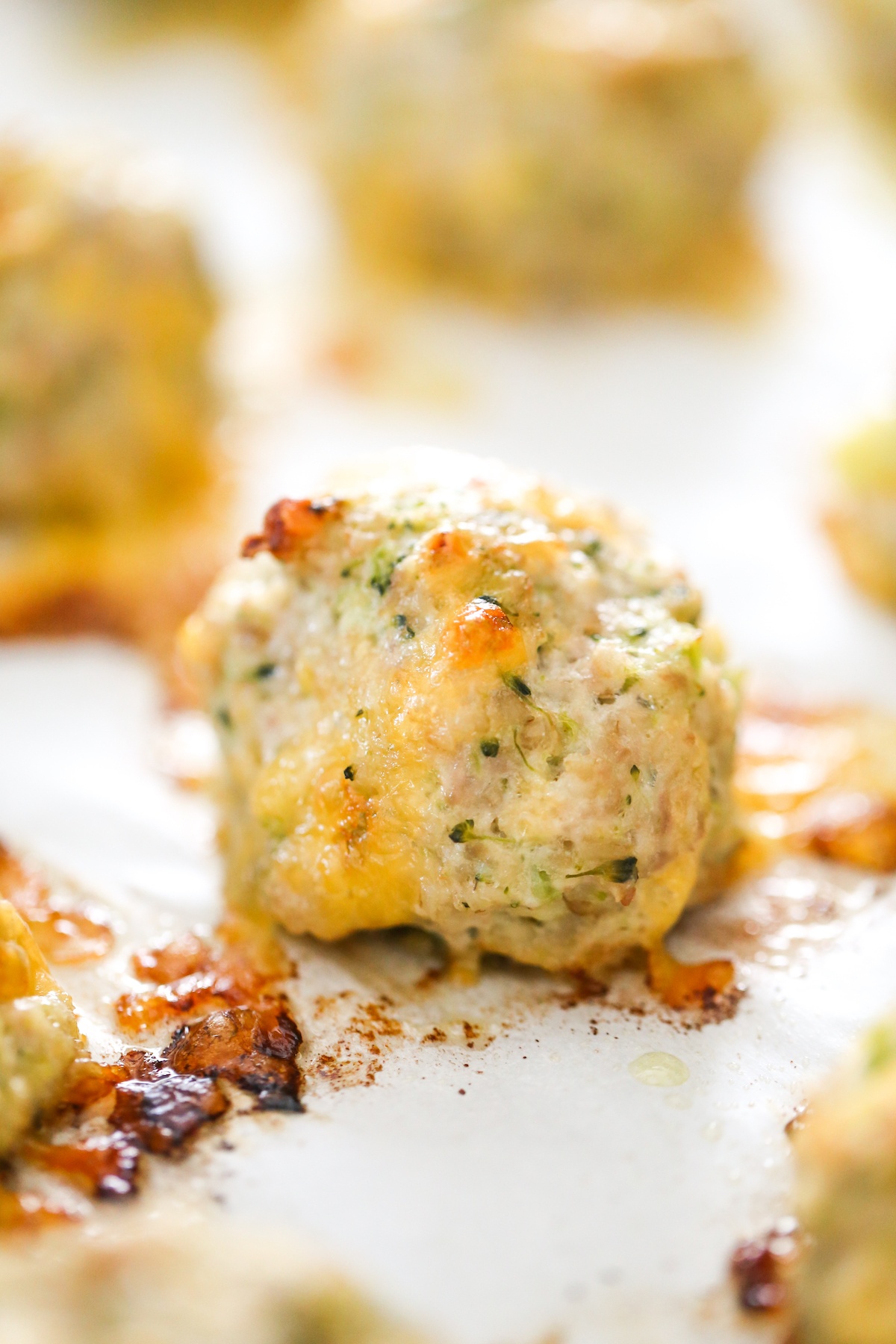 Close up of baked turkey meatballs with broccoli and cheddar cheese on a baking sheet