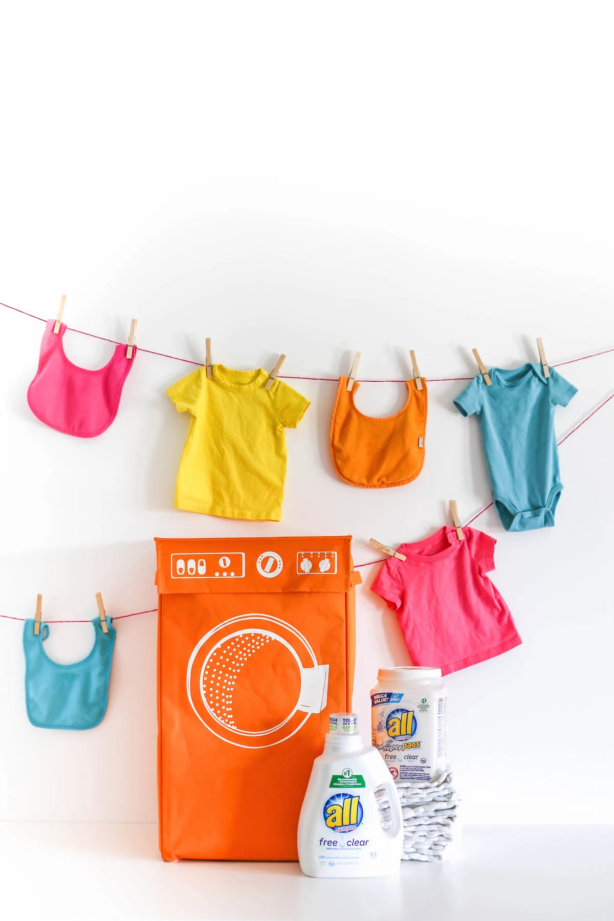 Baby clothes hanging on rope with a hamper and laundry detergent