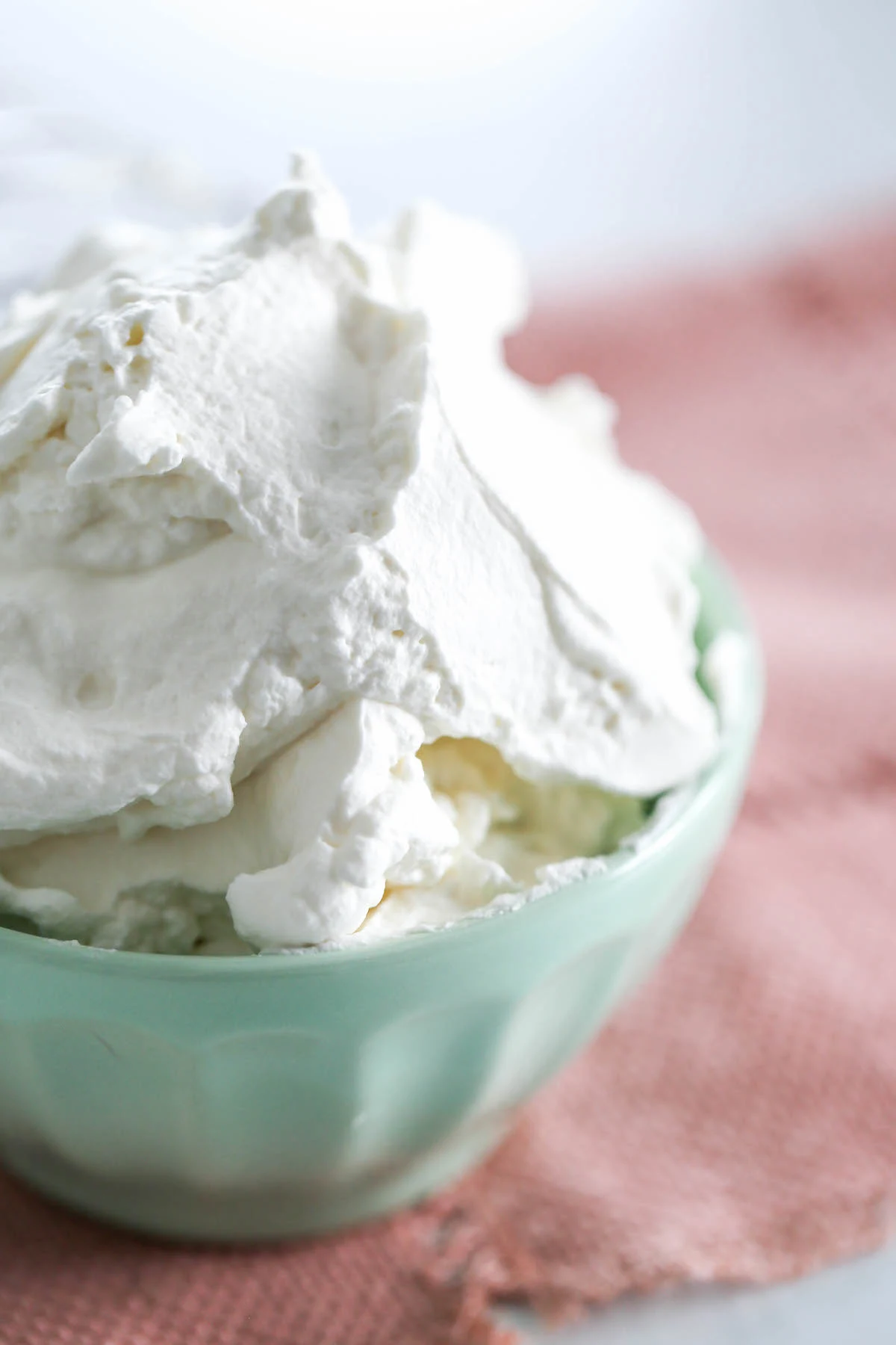 Close up of homemade whipped cream in a mint colored bowl set on a pink placement