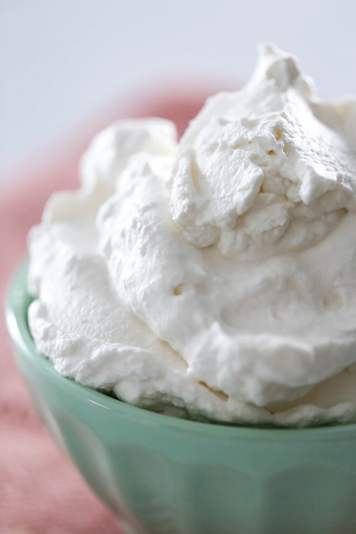 Close up of homemade whipped cream in a mint colored bowl set on a pink placement