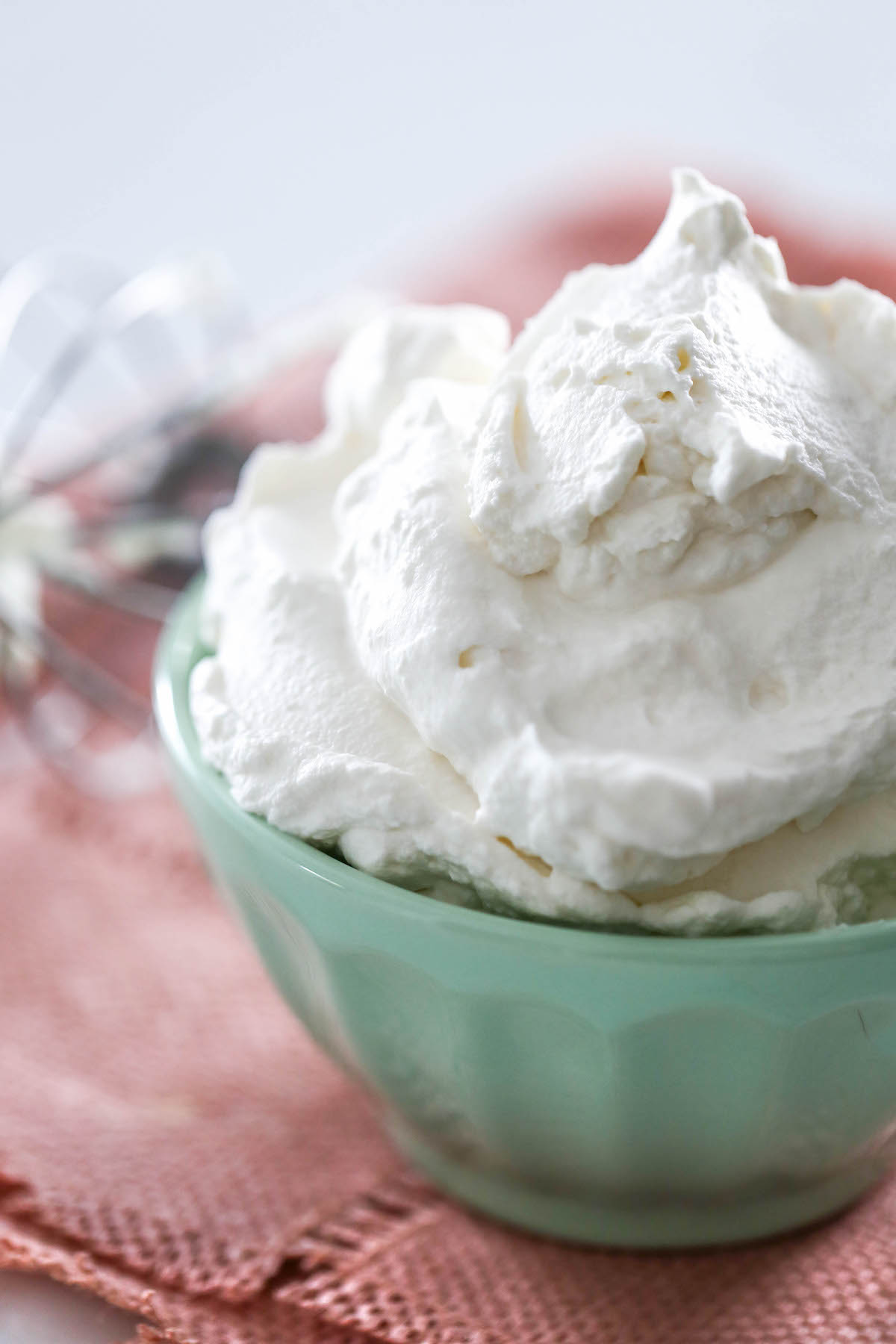 Close up of homemade whipped cream in a mint colored bowl set on a pink placement