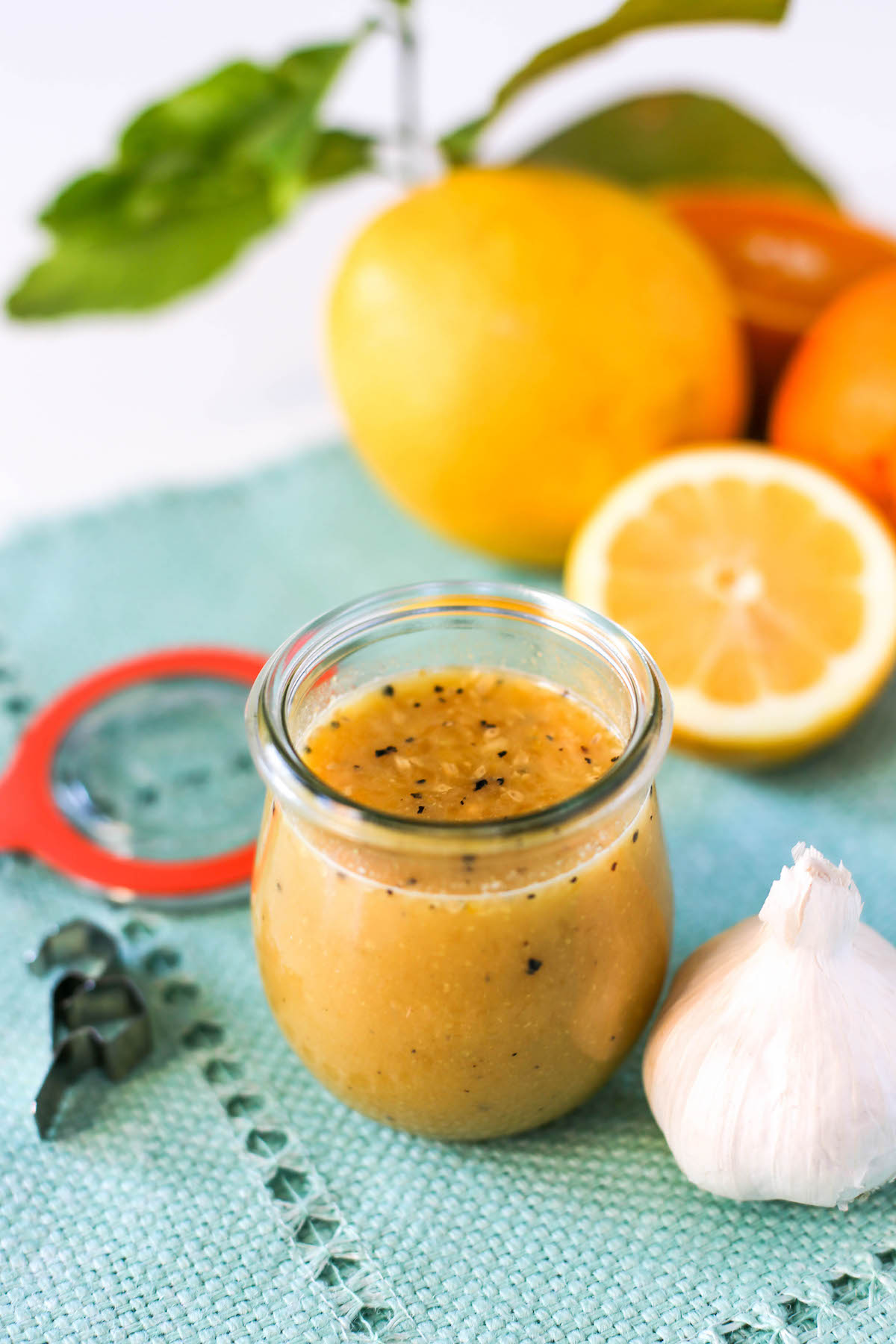 Citrus vinaigrette in a jar atop a blue placemat with lemons, oranges, a head of garlic surrounding it